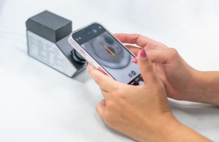 Female hand holding smartphone for taking a photo with the RI of a refractometer to confirm the type of jewelry.